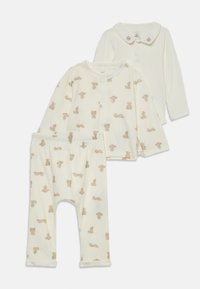 Set med tre babykläder: krämfärgad långärmad topp med nallebjörnstryck, matchande byxor och en enkel krämfärgad topp med björnskalla-detaljer på kragen.