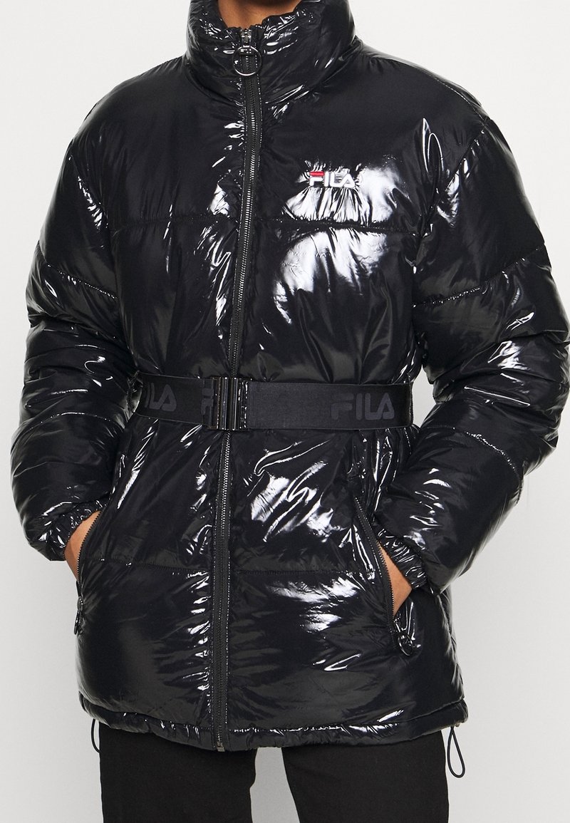 Giacca a vento nera con texture lucida, colletto alto e chiusura con zip. Presenta una cintura nera con il logo FILA e tasche laterali.
