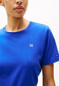 Blå bomull t-skjorte med rund hals, korte ermer og en liten brodert logo på brystet. Jevn tekstur, enkelt design.