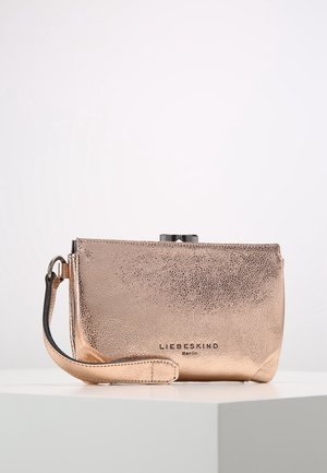 Mała metaliczna różowo-złota kopertówka z paskiem na nadgarstek i logo "Liebeskind Berlin" z przodu, umieszczona na białej powierzchni.