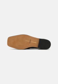 Semelle de chaussure noire avec une base en caoutchouc marron clair, présentant une finition lisse et deux lignes décoratives dorées. Le texte indique "dolce vita."