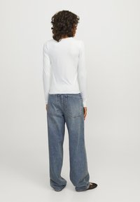 White long-sleeve ribbed top paired with loose blue denim jeans. The top features a scalloped neckline; jeans have a classic five-pocket design.