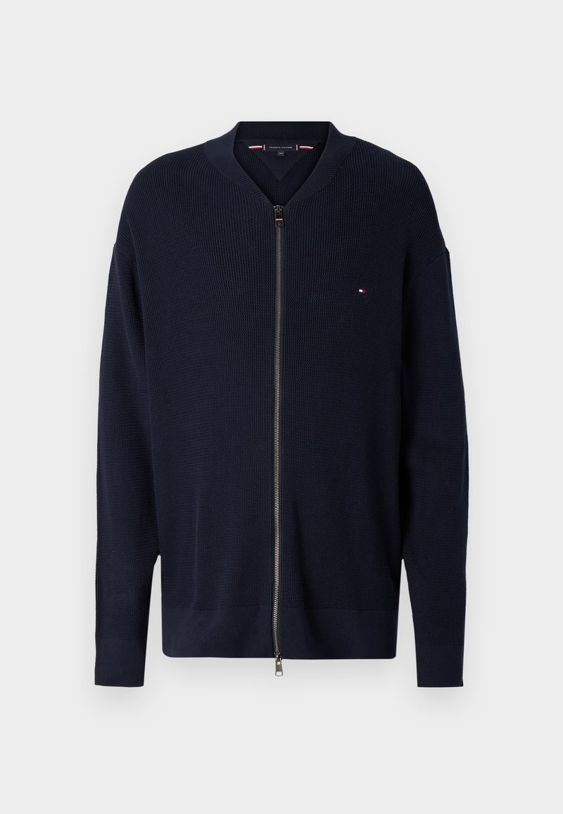 Navy zip-up cardigan with a textured weave, ribbed cuffs, and a V-neck. Features a small logo on the chest and silver zipper hardware.