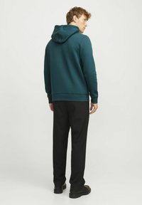 Groene hoodie met een gestructureerde afwerking, voorzien van een trekkoordcapuchon, geribbelde manchetten en onderrand. Gecombineerd met zwarte broeken en schoenen.