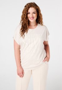 T-shirt beige clair à manches courtes, avec un texte blanc indiquant "Boulevard Saint Germain" et une texture légère chinée.