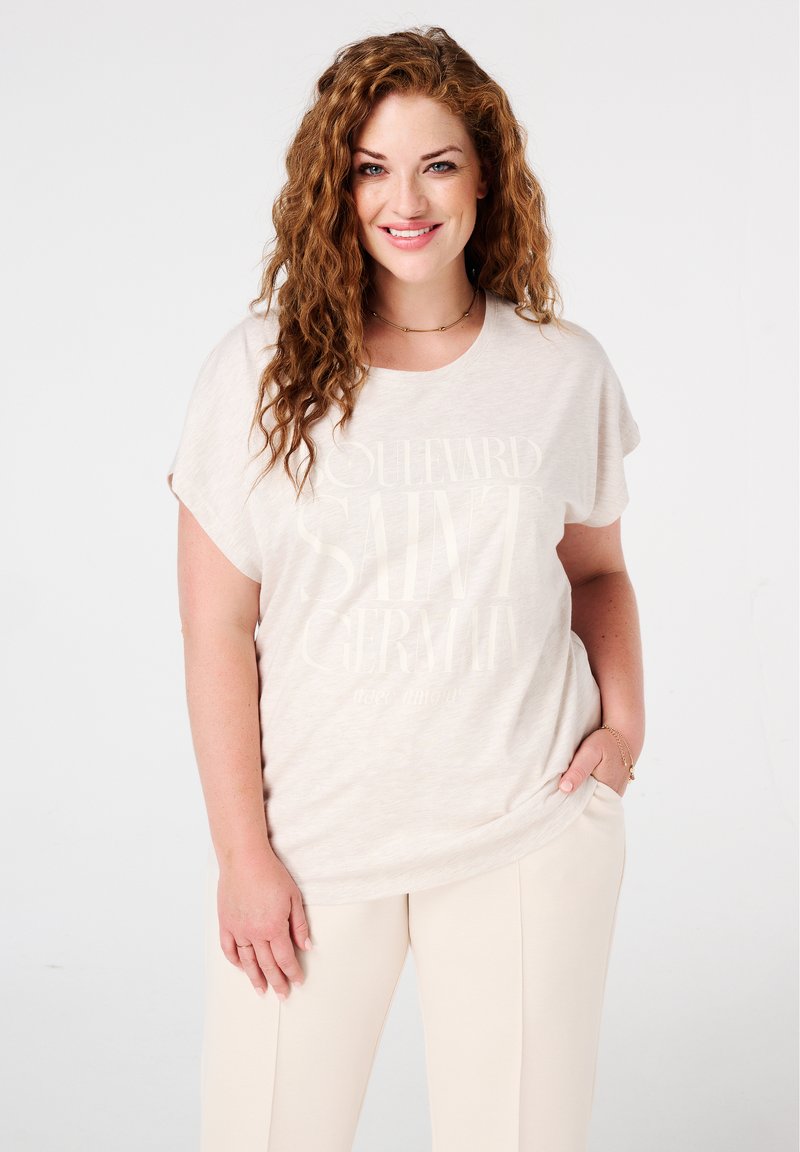 T-shirt beige clair à manches courtes, avec un texte blanc indiquant "Boulevard Saint Germain" et une texture légère chinée.