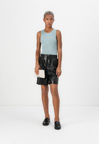 Lichtblauw geribd tanktop, zwarte leren shorts en zwarte loafers; een getextureerde crèmekleurige clutchbag vasthoudend. Eenvoudig, minimalistisch ontwerp.