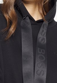 Czarna hoodie z teksturowanej tkaniny, ze sznurkiem do regulacji z wytłoczonym logo "BOSS" oraz luźnym krojem.