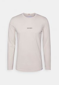 Langärmeliges, hellbeiges Baumwoll-T-Shirt mit einem schwarzen "LES DEUX" Logo in der Mitte. Rundhalsausschnitt und weicher Stoff.