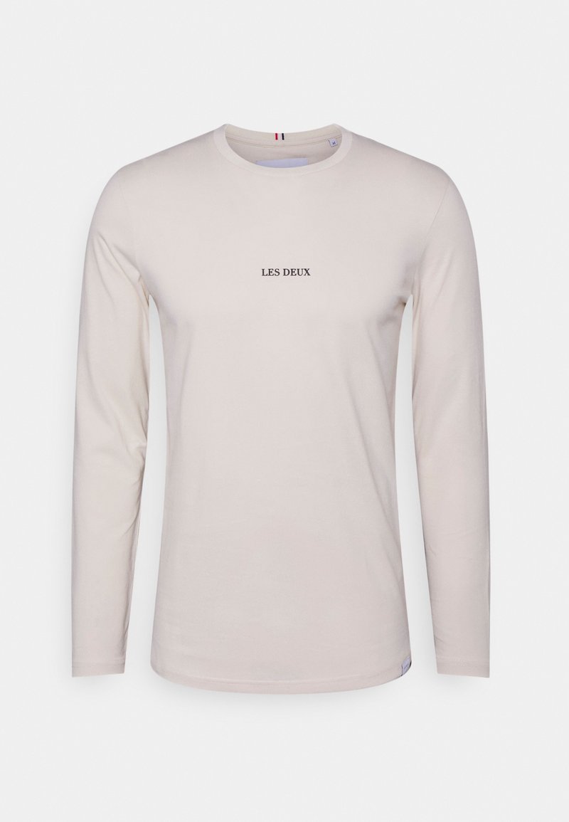 Langärmeliges, hellbeiges Baumwoll-T-Shirt mit einem schwarzen "LES DEUX" Logo in der Mitte. Rundhalsausschnitt und weicher Stoff.