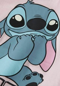 Gros plan sur un extraterrestre bleu en cartoon avec de grands yeux, des oreilles internes roses et des pattes près de sa bouche sur un fond rose clair.