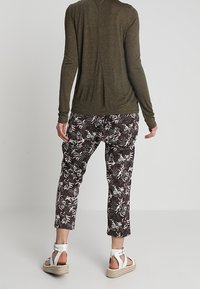 Olijfgroen langemouwtop, lichtgewicht stof; zwarte broek met bloemenpatroon en taps toelopende zoom; witte sandalen met bandjes en espadrillezolen.