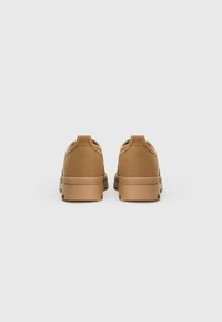 Bruine canvas schoenen met een gestructureerde bovenkant, ronde neus en een duurzame rubberen zool. Eenvoudig ontwerp met minimale stiksels en een aantrekband aan de achterkant.