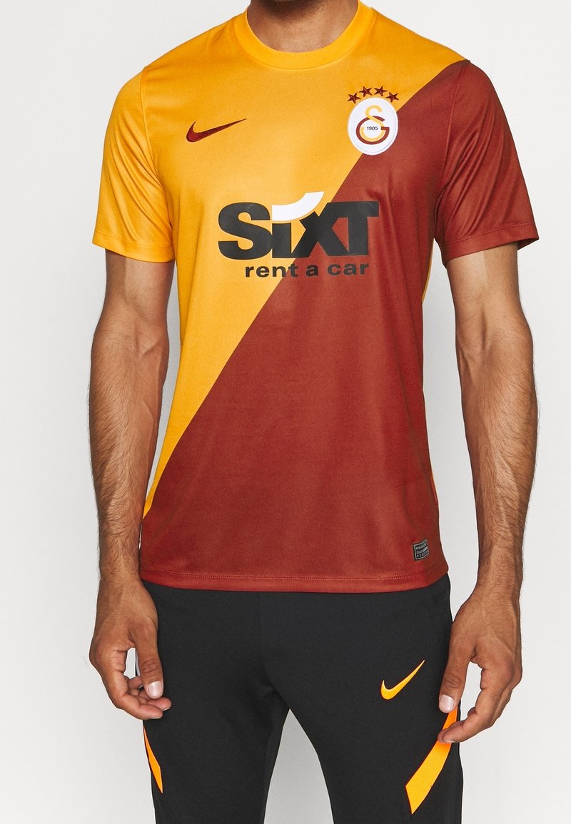 Homme portant un maillot de football Galatasaray jaune et rouge moitié-moitié avec le logo Sixt rent a car et un pantalon Nike noir.