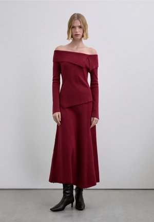 Conjunto de dos piezas de punto burdeos con top de hombros descubiertos y falda larga, acabado texturizado, bordes ondulados, combinado con botas marrones hasta la rodilla.