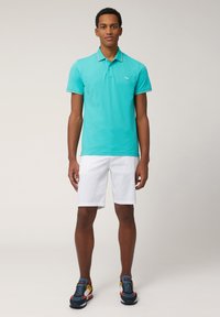 Turquoise polo shirt with a collar, short sleeves, and a small logo. Paired with white shorts and multicolored athletic shoes.