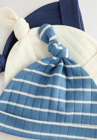 Trois bonnets tricotés : bleu foncé, crème avec de fines rayures verticales, et bleu clair avec des rayures horizontales. Chacun a un nœud noué sur le dessus.
