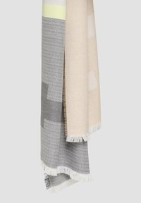 Couverture tissée en gris et beige clair, présentant des motifs en zigzag et en grille, avec des bords frangés pour plus de texture et de détails.