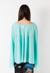 Blusa in chiffon color acquamarina chiara con scollatura ampia e maniche flottanti, caratterizzata da una texture traslucida e leggera.