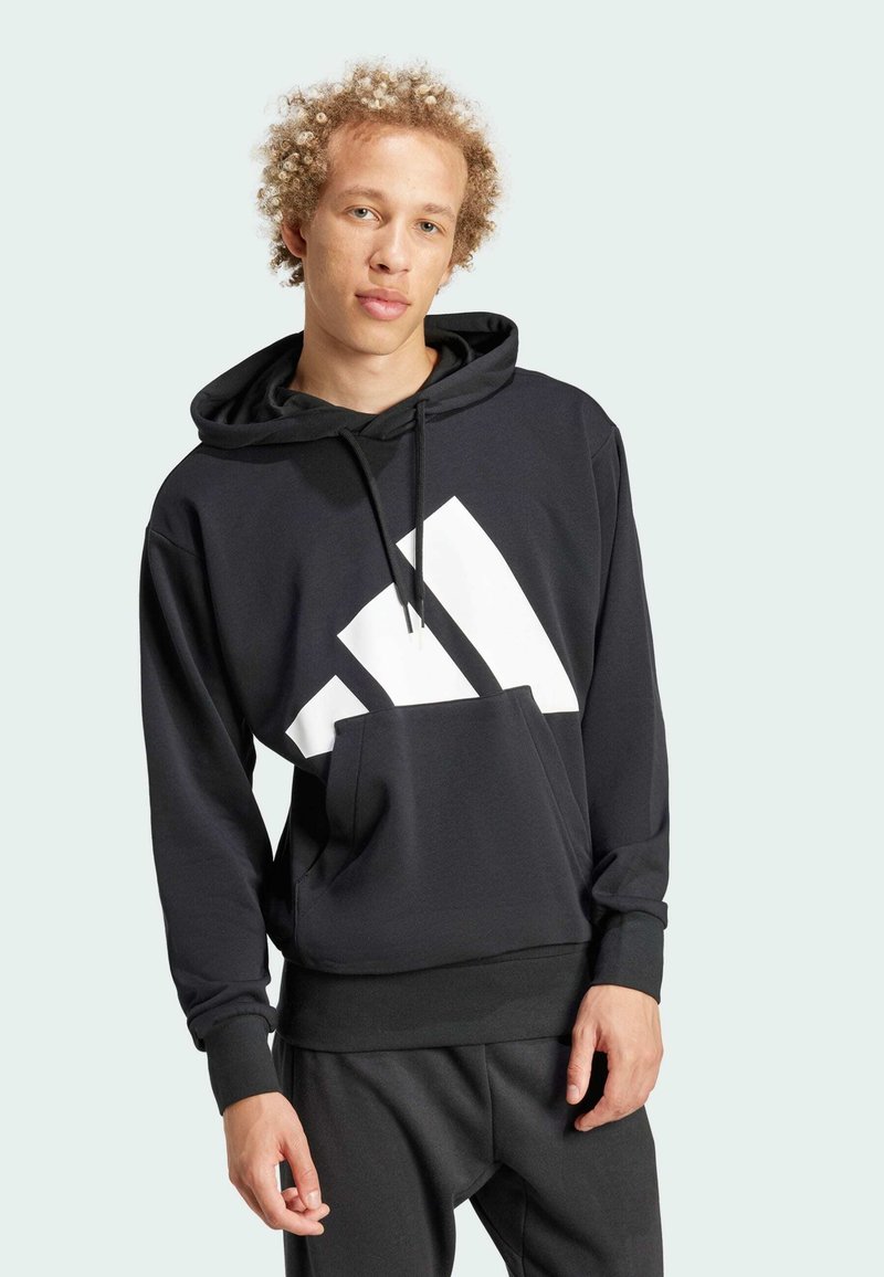 Black hooded sweatshirt with a large white logo, Kangaroo pocket, ribbed cuffs and hem, made of soft fabric. Worn with matching pants.