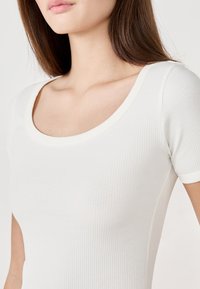 Top bianco a maniche corte a costine con scollatura rotonda e texture liscia, che presenta un design aderente e cuciture sottili.