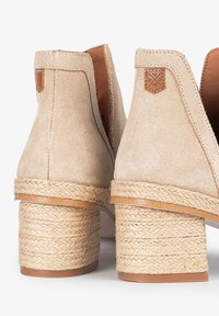 Botas de tobillo de ante beige con tacones de yute trenzado y acentos de cuero; textura suave con forma redondeada y detalles de costura mínimos.