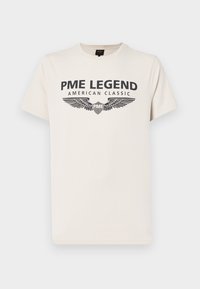 Kremna bombažna majica s temnim potiskom, ki na njej piše "PME LEGEND AMERICAN CLASSIC" z grafiko kril pod besedilom.