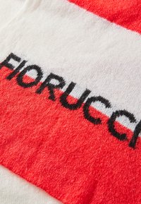 Piros és fehér csíkos textil, amelyen fekete hímzett szöveg olvasható: "Fiorucci." Az anyag lágynek tűnik, textúrált, enyhén bolyhos felülettel.