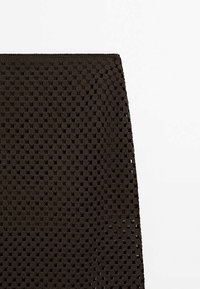 Brauner gestrickter Stoff mit einem strukturierten, offenen Webmuster. Das Design zeigt ein Gitter aus kleinen, abgerundeten Formen und eine gerade Kante.