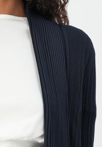 Navy ribbed cardigan with a relaxed fit, featuring a structured texture and open front design, layered over a plain white top.