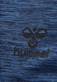 Logo de Hummel en negro sobre un fondo de tela texturizada azul.