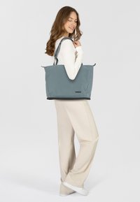 Tote bag Thule grise en matériau lisse et imperméable, dotée d'une fermeture zippée, de poignées doubles et d'une base noire contrastante.