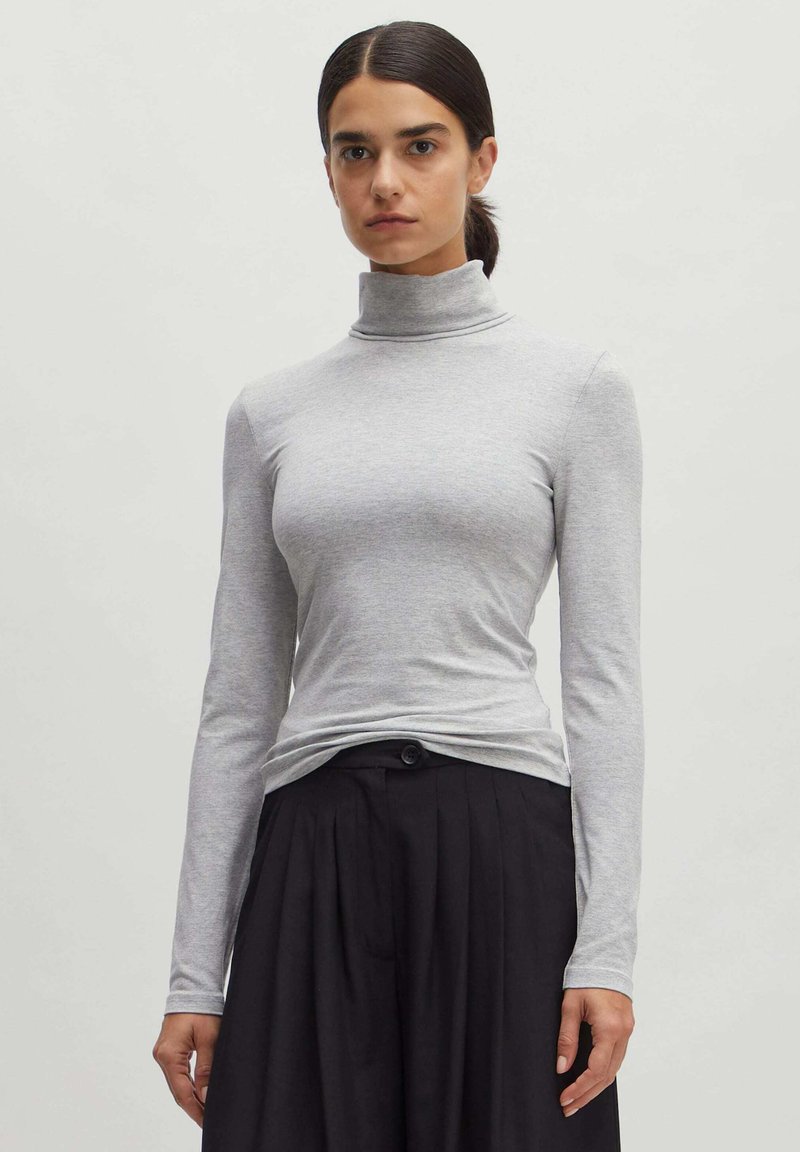 Grijze lange mouwen coltrui met een slim fit en zachte textuur, gecombineerd met zwart hooggeprofileerd geplooid broek, met knoopdetail zichtbaar.