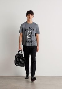 Grå grafisk t-shirt med ett motiv som har texten "BLACK WIDOW". Bärs med svarta byxor och en svart väska. Svarta skor fulländar outfiten.