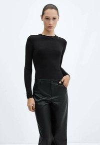 Top nero a maniche lunghe realizzato in tessuto morbido, design aderente. Abbinato a pantaloni in finta pelle nera lucida a vita alta.