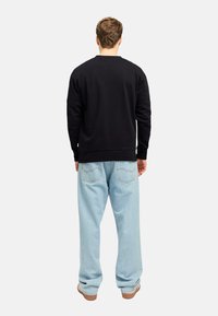 Sudadera negra de cuello redondo con mangas largas, combinada con unos vaqueros sueltos de color azul claro. Estilo casual con una silueta relajada.