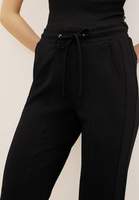 Pantalons de jogging noirs en tissu doux, dotés d'une taille élastique avec cordon de serrage, de poches latérales et d'une coupe décontractée.
