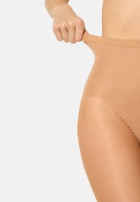 Beige højtaljede trusser lavet af glat stof med en sømløs konstruktion og elastik i taljen. Hånden trækker i taljebåndet.