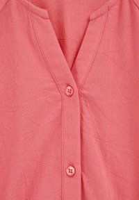 Nahaufnahme eines pinkfarbenen V-Ausschnitts mit sichtbaren Nähten und zwei passenden Knöpfen entlang der vorderen Blende.