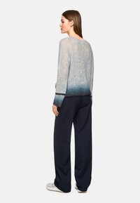 Leichter Pullover mit einem Verlauf von Hellgrau zu Dunkelblau, der einen lässigen Schnitt und eine subtile Textur aufweist. Kombiniert mit navyblauen Weitbein-Hosen.