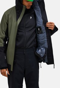 Wasserdichte Jacke mit einem dunkelgrünen und schwarzen Design, ausgestattet mit einem gesteppten grauen Futter und einem Etikett, das die "HIPE"-Technologie anzeigt.