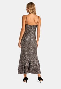 Sukienka wieczorowa na ramiączkach, długości do podłogi, w srebrne i czarne cekiny, dopasowana góra, rozkloszowany dół z rozcięciem z tyłu, w zestawie z czarnymi szpilkami.