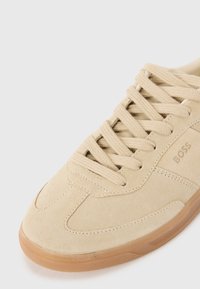 Sneaker in suede beige con superficie testurizzata, lacci piatti e suola in gomma naturale. Presenta un discreto logo del marchio in rilievo sul lato.