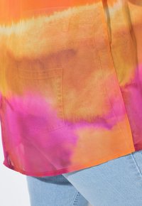 Top trasparente con tie-dye che presenta sfumature degradanti di arancione, rosa e giallo, con orlo dritto e un sottile dettaglio sulla tasca.
