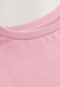 Maglietta rosa a maniche corte con scollo rotondo. Il tessuto ha una texture liscia con una lieve lucentezza e cuciture pulite intorno al colletto.