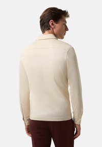 Lange mouwen, collared shirt in crèmekleurige stof, met een gladde textuur, getailleerde pasvorm en geknoopte manchetten. Gedragen met donkere broeken.