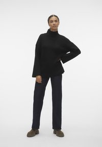 Svart, oversized høyhalset genser med teksturert finish, kombinert med mørkeblå rette jeans og brune ankelstøvler.