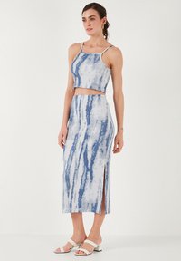 Modrý a bílý tie-dye crop top a midi sukně vyrobené z měkké tkaniny, s bočními rozparky a tenkými ramínky, v kombinaci s bílými sandály na podpatku.