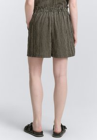 Pantaloni corti a righe marroni e crema con vita elastica, tasche laterali e vestibilità comoda, abbinati a scarpe slip-on scure.