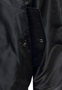 Sort jakkeærme tæt på, der viser en knappelomme med syningsdetaljer og glat, let skinnende stoftekstur.